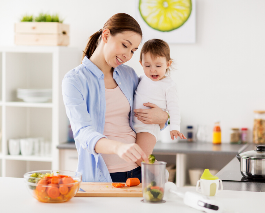 A mother holds her toddler on her hip and is preparing healthy food.